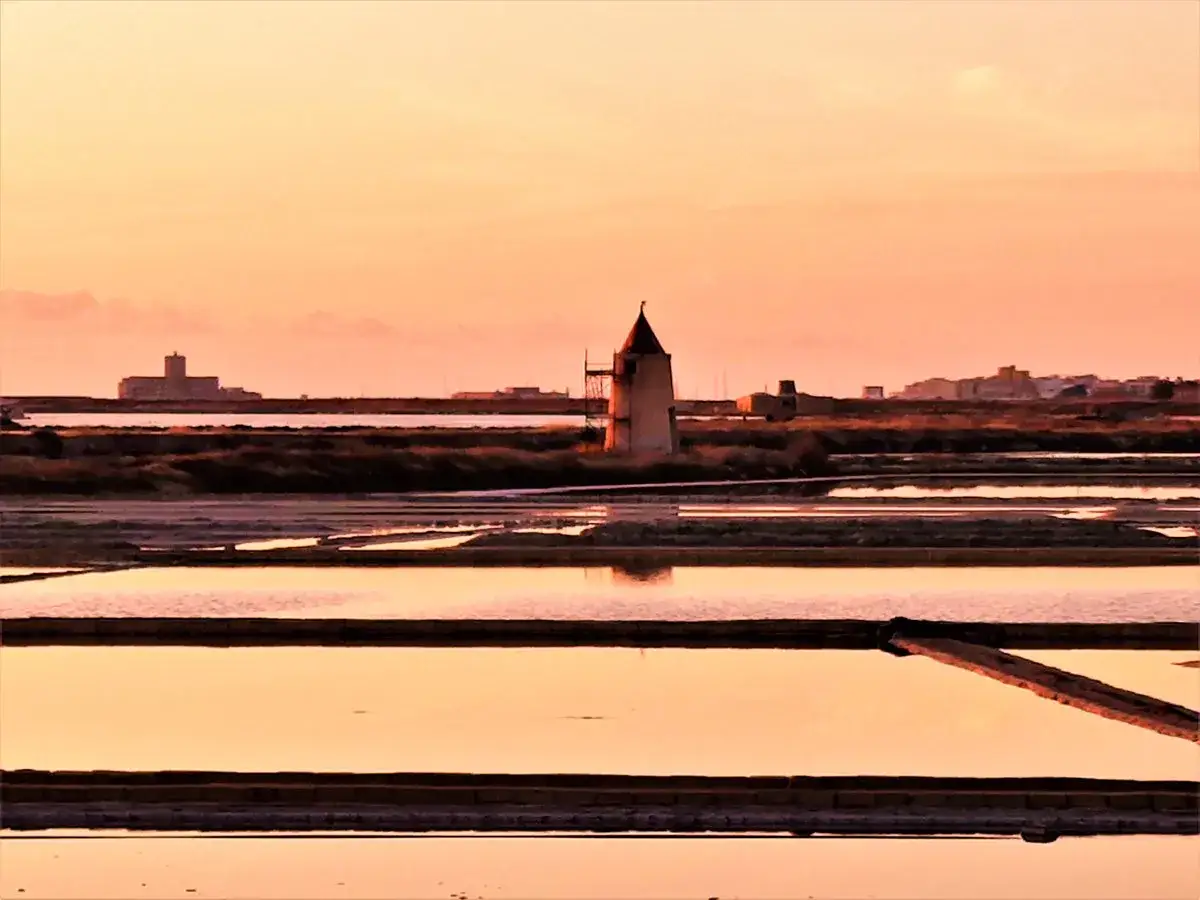Saline di Trapani al tramonto, con mulino a vento. Un'ottima idea per le cose da fare a Trapani, ammirando la natura.