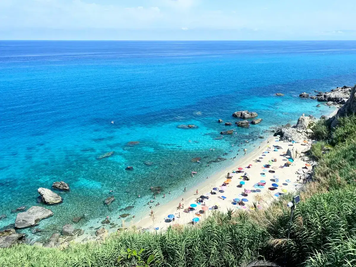 Spiagge calabresi baciate da un mare cristallino, con ombrelloni colorati e bagnanti che si godono il sole.