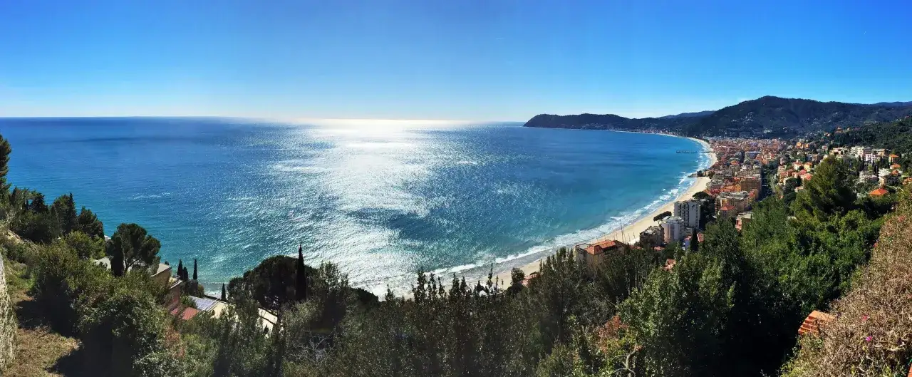 Vista panoramica di una costa ligure con mare azzurro, spiagge dorate e case colorate. Un paesaggio da cartolina tra le spiagge più belle Liguria.