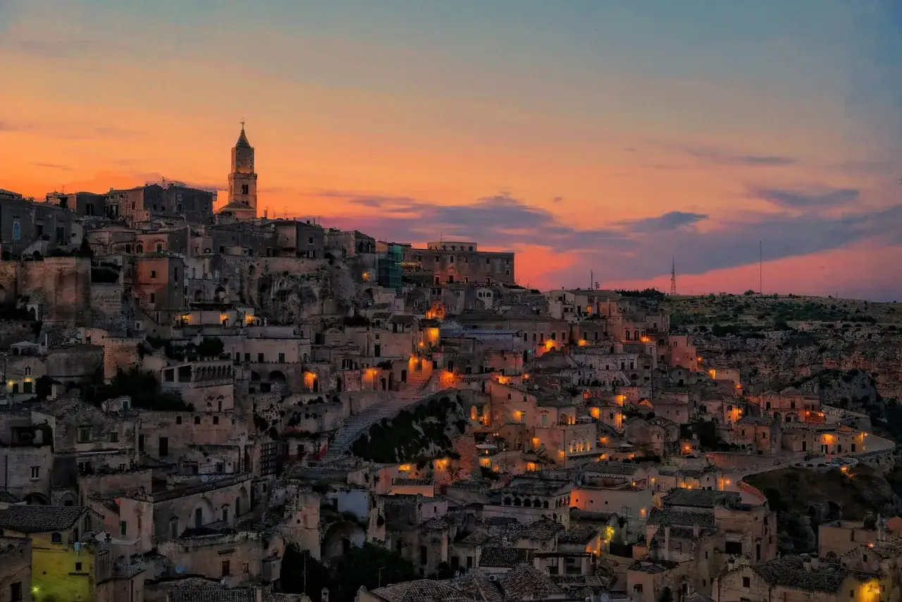 Un suggestivo itinerario a Matera: i Sassi illuminati al tramonto, con il cielo che sfuma tra arancio e blu, creano un'atmosfera magica.