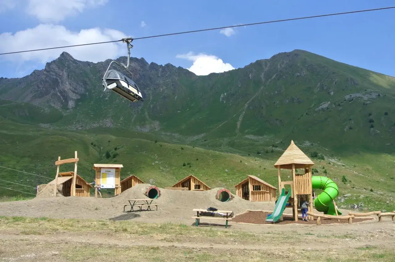 Un parco giochi alpino, al villaggio delle marmotte, con scivoli, tunnel e una seggiovia in movimento.