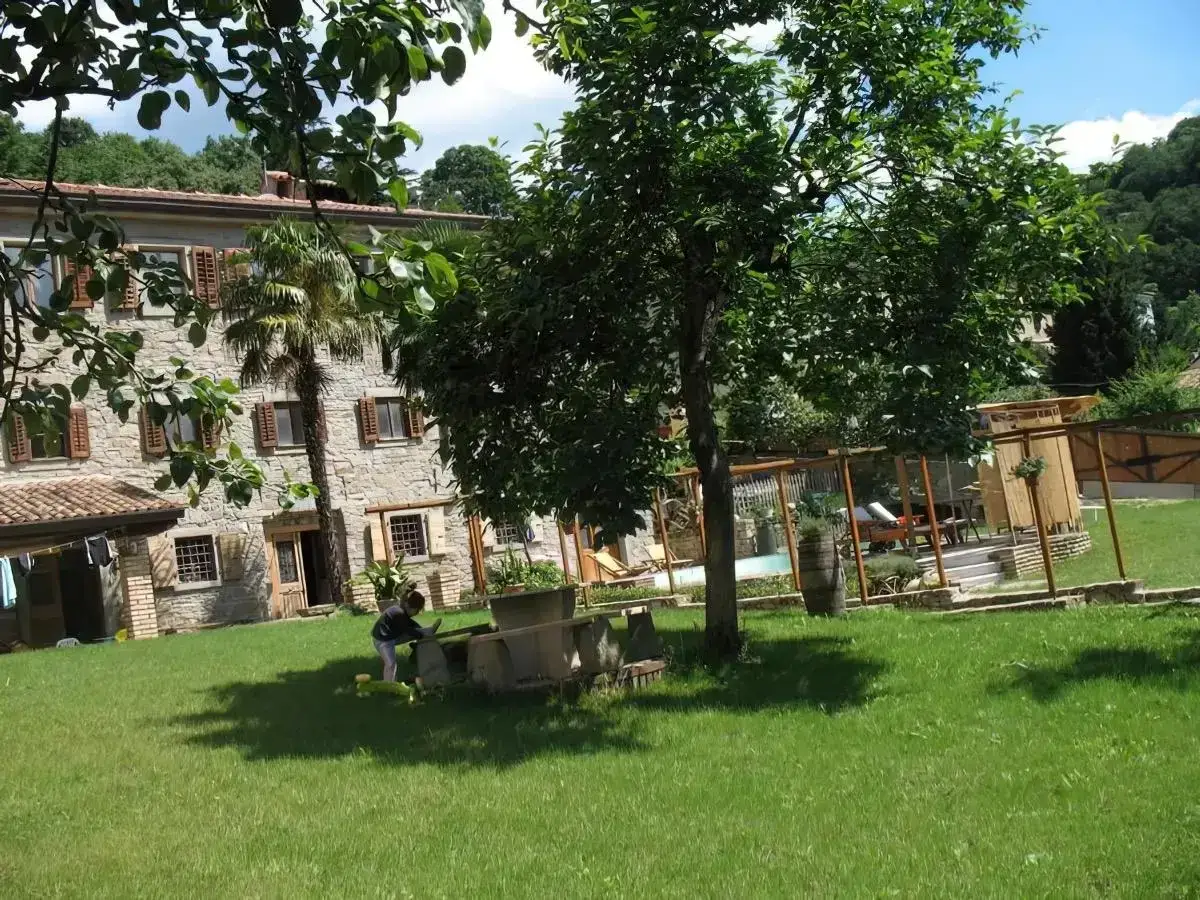 Un bambino gioca nel prato di un agriturismo al Selvadigo, con una casa in pietra e alberi rigogliosi.