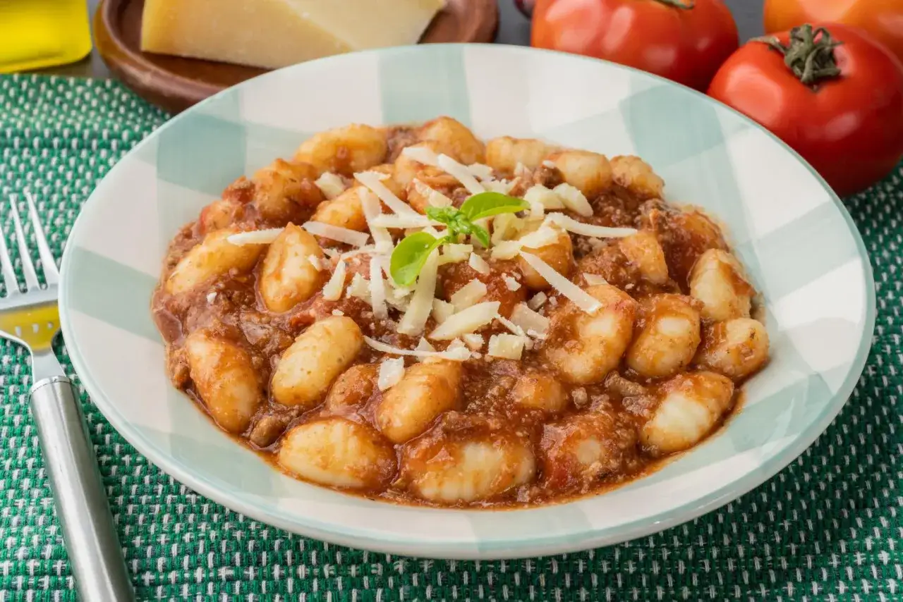 Gnocchi al ragù, un classico tra i piatti tipici di Perugia, serviti in un piatto con parmigiano grattugiato e basilico.