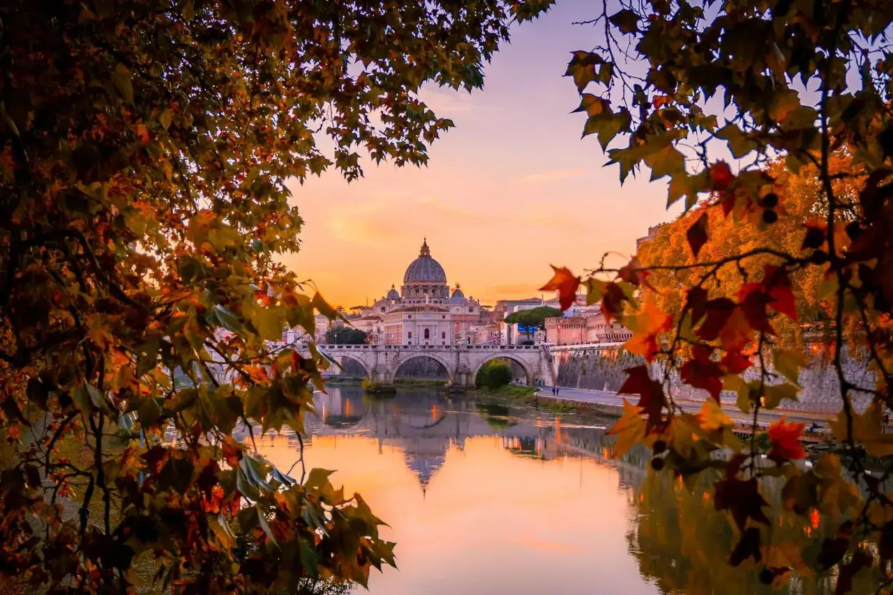 Roma in autunno, con le foglie dorate che incorniciano la cupola di San Pietro e il Tevere riflesso. Una delle città da visitare a novembre per un'atmosfera magica.