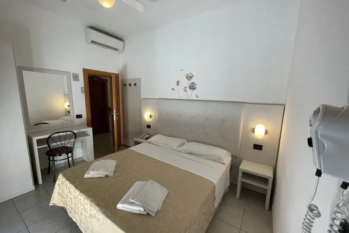 Camera accogliente con letto matrimoniale, specchio e asciugacapelli. Perfetta per chi cerca hotel Marina Riccione recensioni positive.