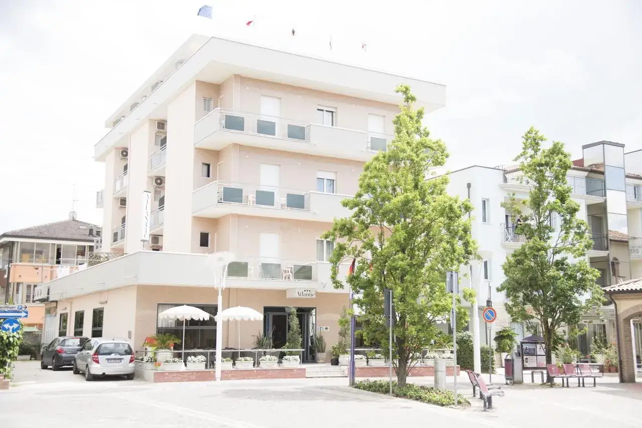 Hotel Atlantic Igea Marina: scopri i prezzi per la tua vacanza al mare. Edificio moderno con alberi verdi davanti.