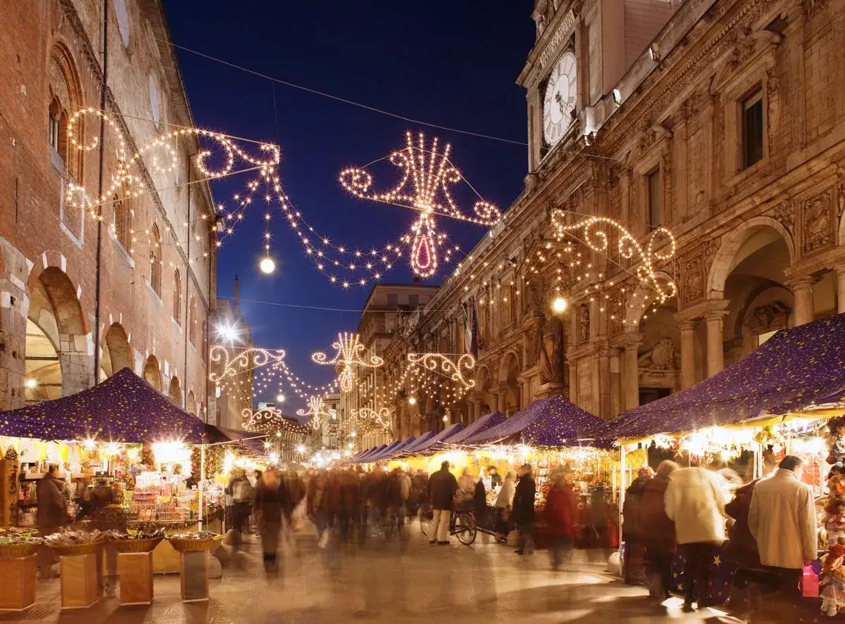 Una strada illuminata da lucine natalizie, con bancarelle e gente che passeggia: ecco i mercatini di Natale più belli.