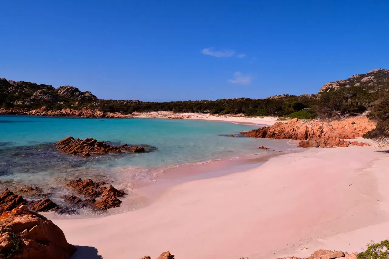 Spiaggia rosa di Asinara, con rocce rosse e mare turchese sotto un cielo azzurro.