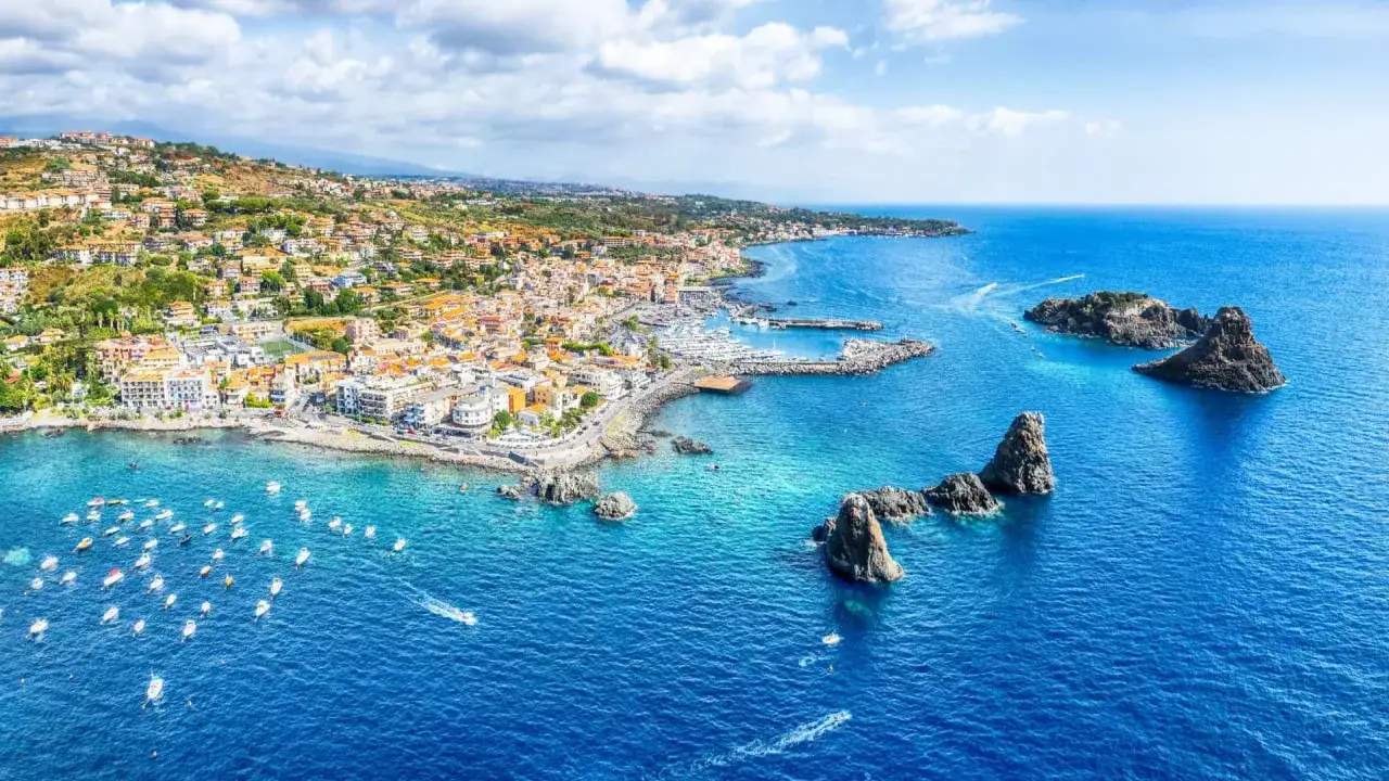 Vista aerea di un pittoresco borgo costiero con case colorate, un porto turistico e faraglioni. Un'ottima idea per le citt&agrave; da visitare ad agosto.