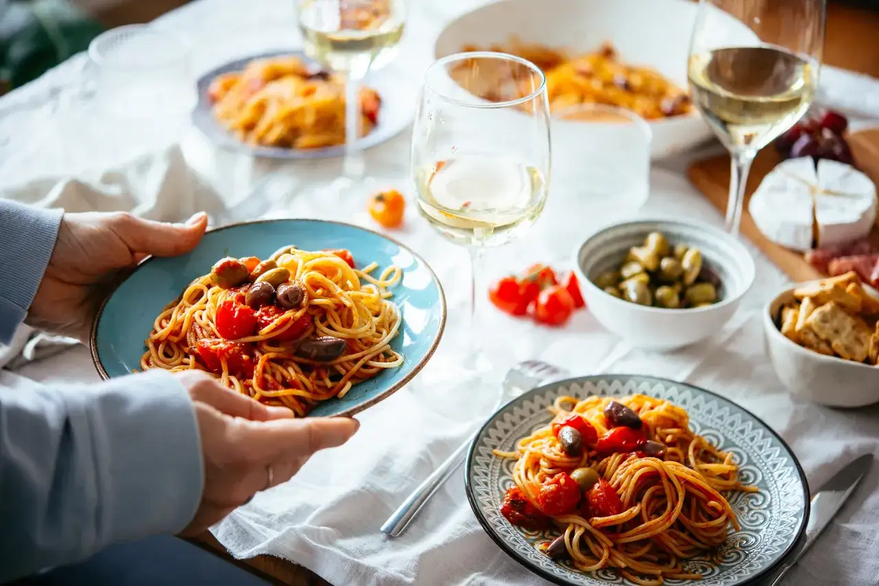 Un piatto di spaghetti al pomodoro e olive, un classico su cosa mangiare in Italia. Servito con vino bianco e contorni.