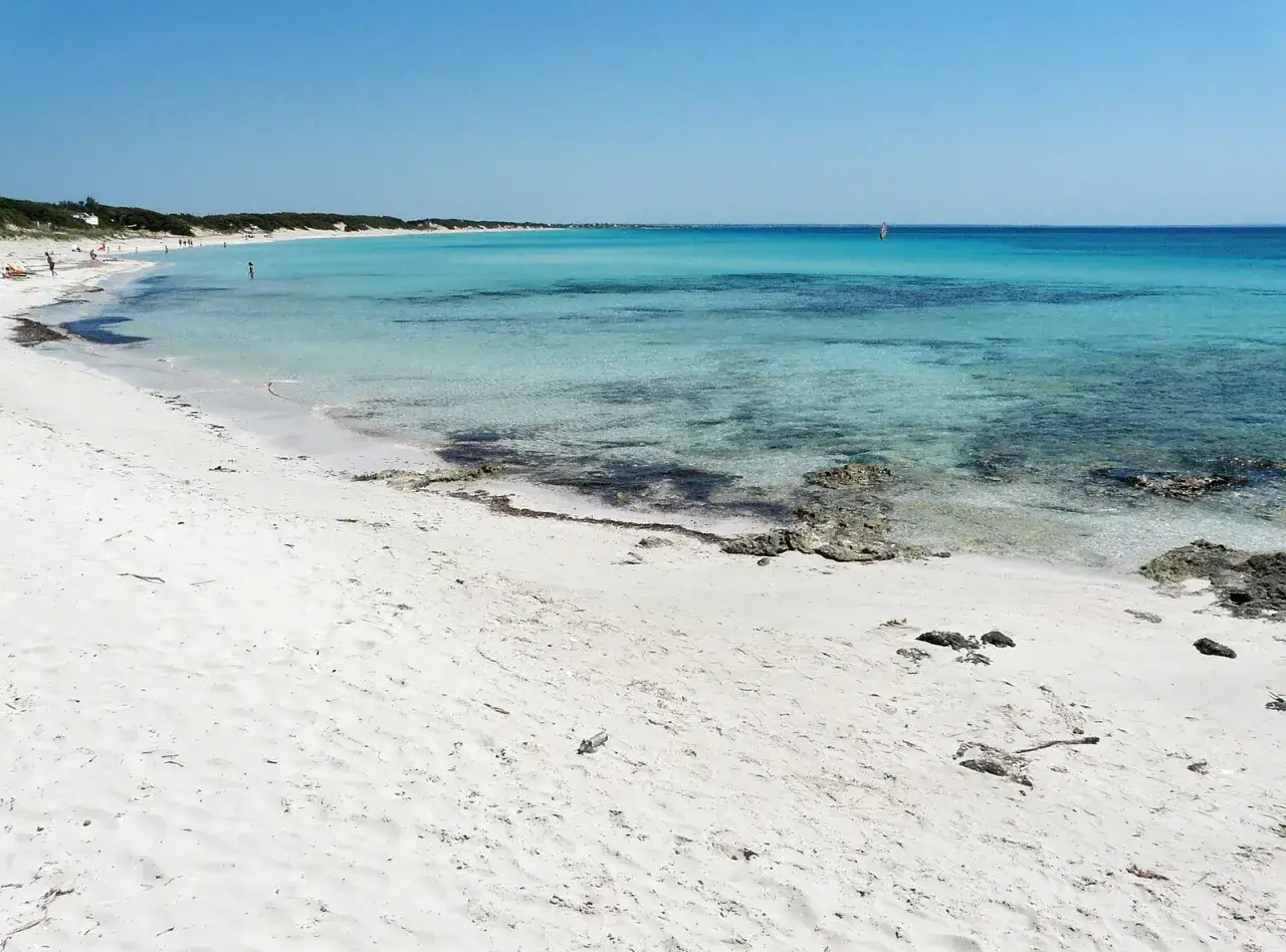 Spiaggia bianca e mare cristallino del mar Ionio in Puglia, con un windsurfista all'orizzonte.