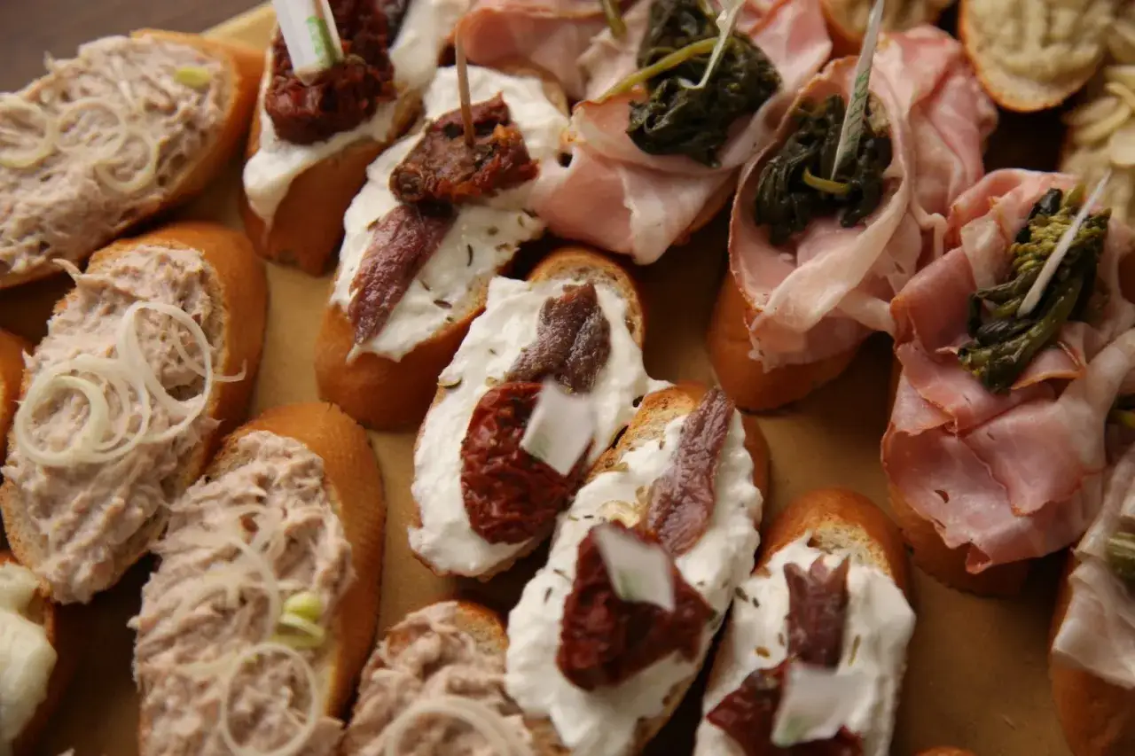 Cosa mangiare a Venezia? Assaggia questi cicchetti: crostini con tonno, acciughe, pomodori secchi e prosciutto.