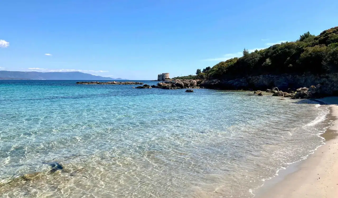 Acque cristalline e sabbia dorata sulle spiagge di Alghero, con una torre antica che veglia sul mare turchese.