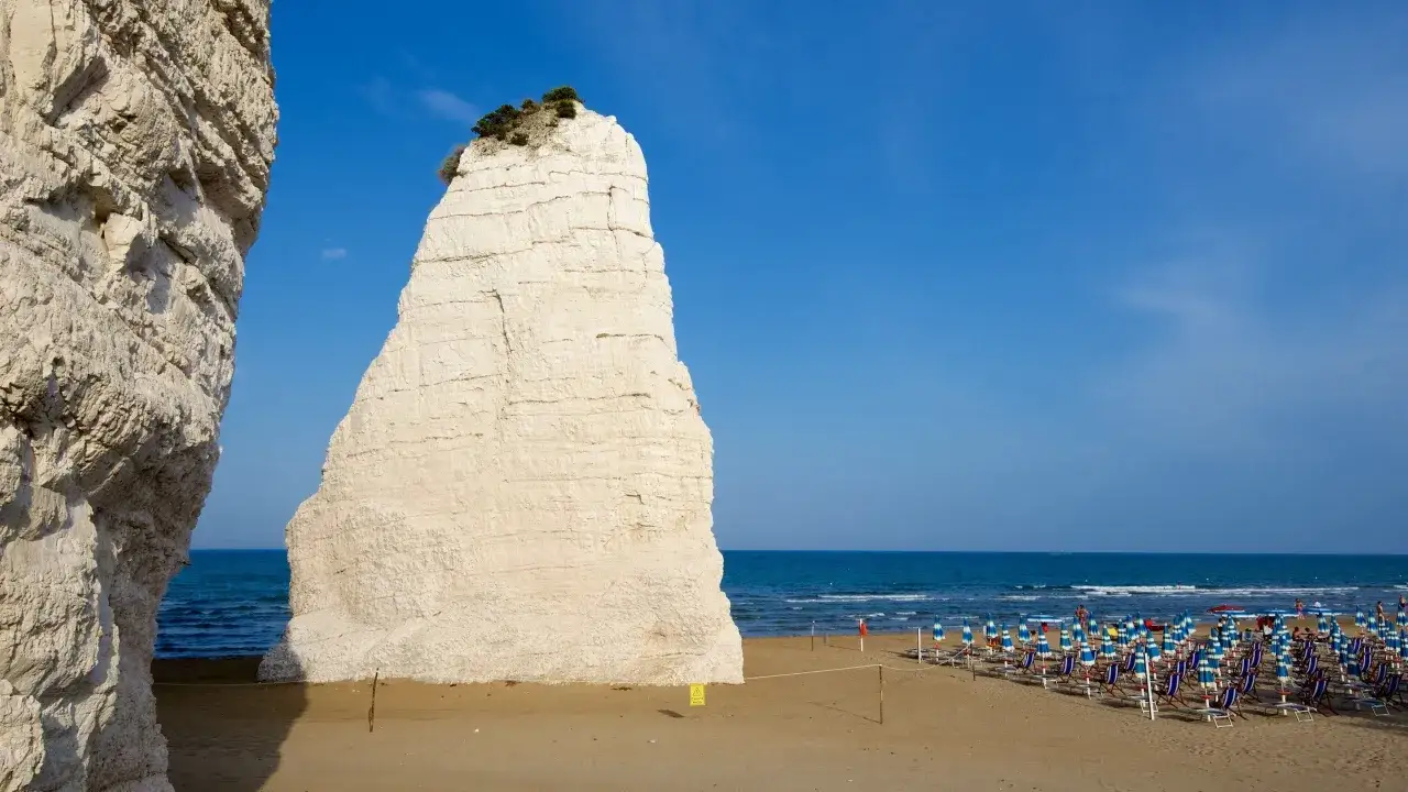 Scogliera imponente e spiaggia attrezzata a Ripa Beach Vieste, con ombrelloni e lettini pronti per accogliere i bagnanti sotto il cielo azzurro.