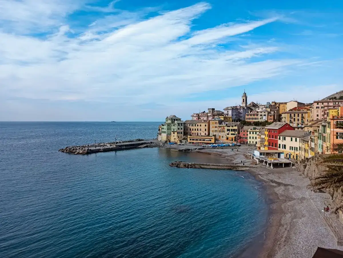 Colorate case affacciate sul mare blu delle coste liguri, con un molo e una spiaggia di ciottoli.