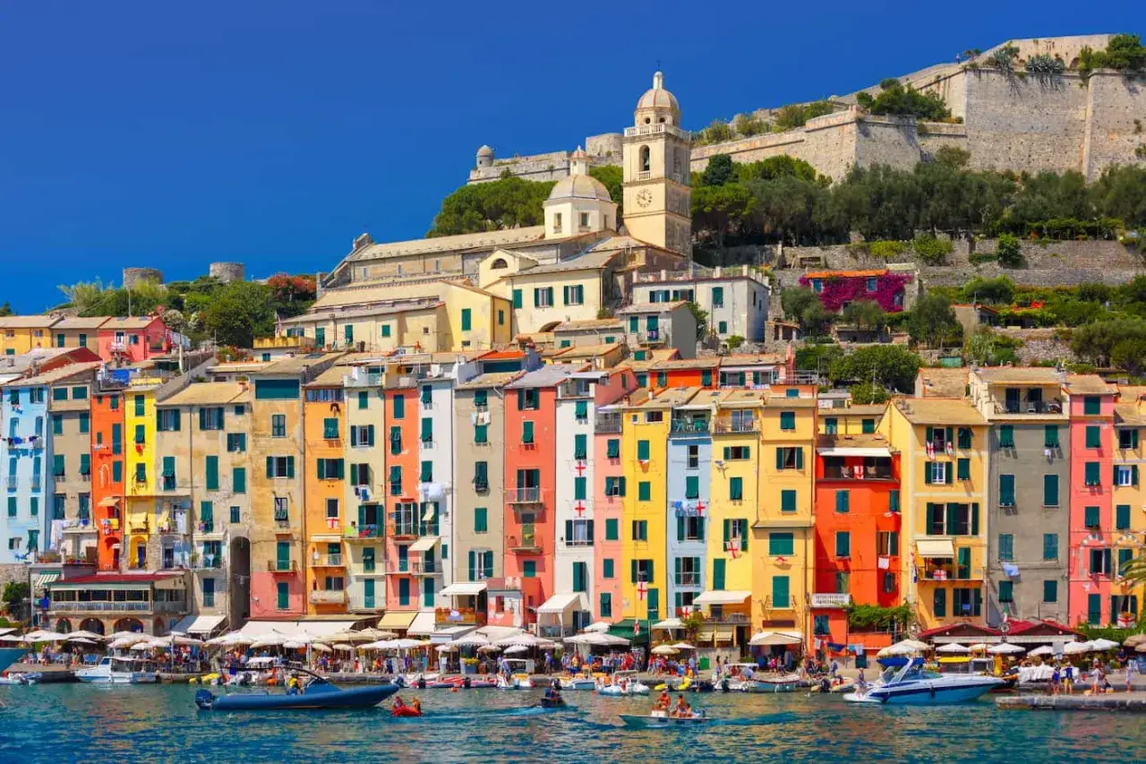 Colorate case affacciate sul mare nel portovenere centro storico, con una chiesa e un castello in collina.