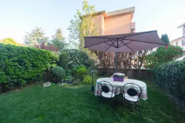 Un giardino curato con tavolo, sedie e ombrellone, circondato da siepi e alberi. Sembra l'albero dei gufi, un luogo magico per rilassarsi.