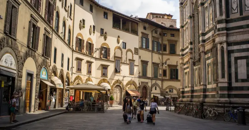 Un gruppo di turisti con valigie a rotelle cammina in una piazza fiorentina, un'immagine perfetta per un **viaggio in Toscana**.