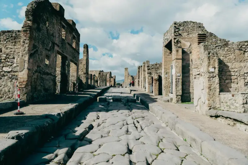 Antica strada romana a Pompei, con rovine di edifici e turisti che passeggiano. Un'ottima guida per come visitare Pompei.
