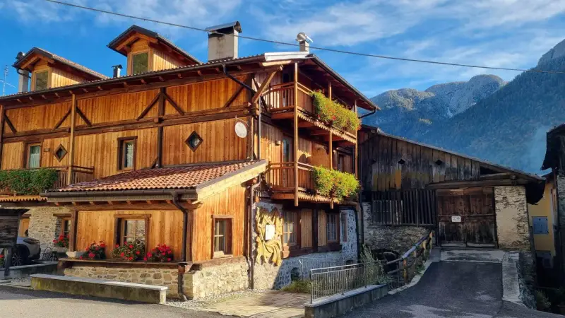 Casa in legno con balconi fioriti e montagne sullo sfondo. Un cartello "Alle Meridiane" indica un luogo incantevole a Lagopesole.